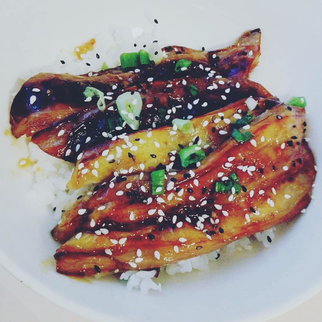 fried eggplant slices peppered with green onion and sesame seeds, on a bed of rice